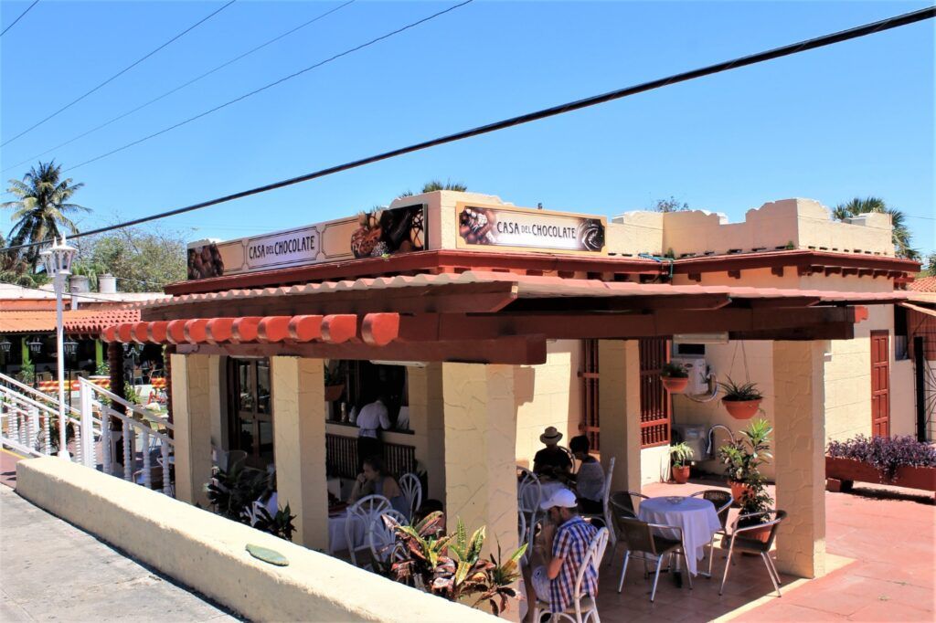 People sitting at outdoor tables under a shaded terrace at 'Casa del Chocolate' in Cuba.