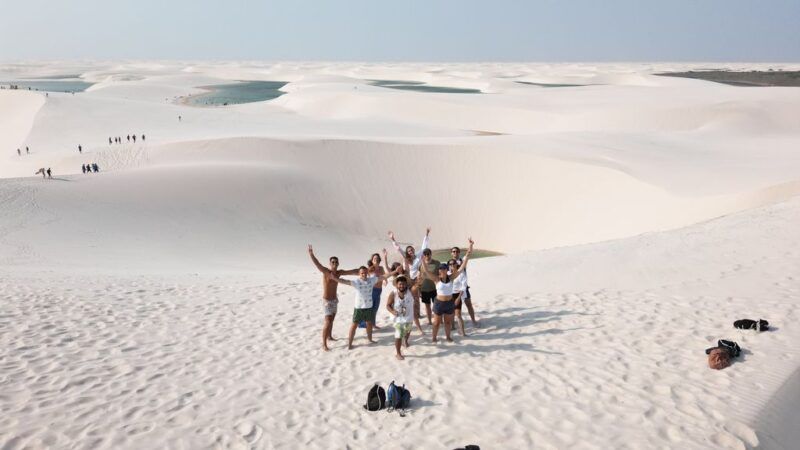 WeRoad travelers enthusiastically posing on the white sand dunes of the Lençóis Maranhenses National Park in Brazil.