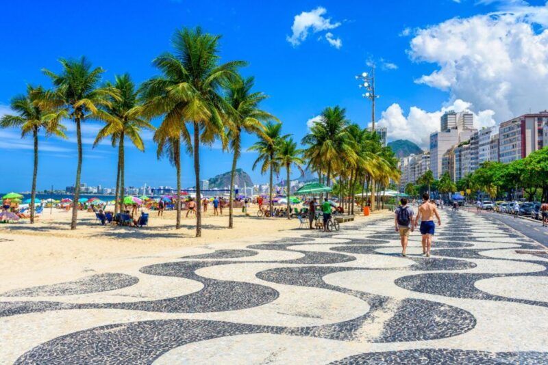 Promenade of Copacabana with its iconic mosaics, lined with palm trees and the beach under a blue sky in Rio de Janeiro.