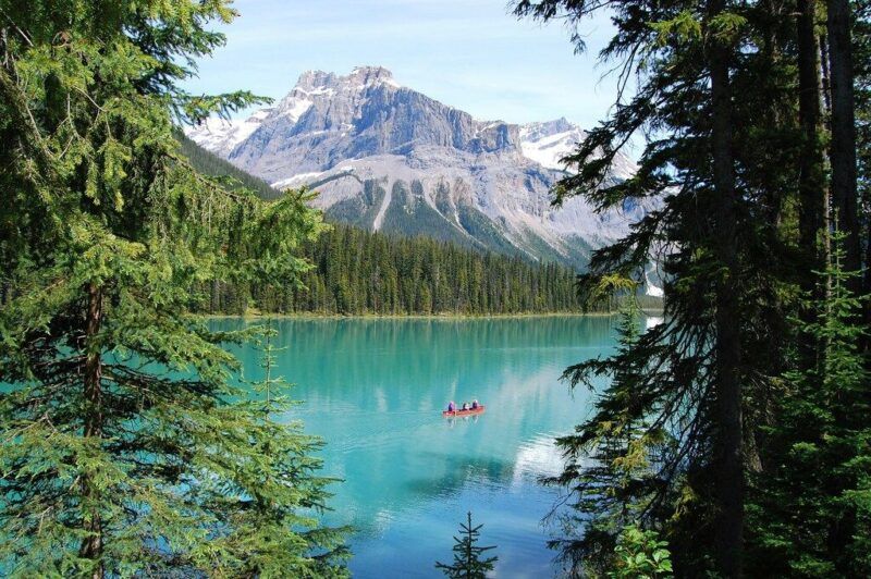 A red canoe on the turquoise waters of Emerald Lake in Canada, framed by green pine trees and majestic snow-capped mountains.