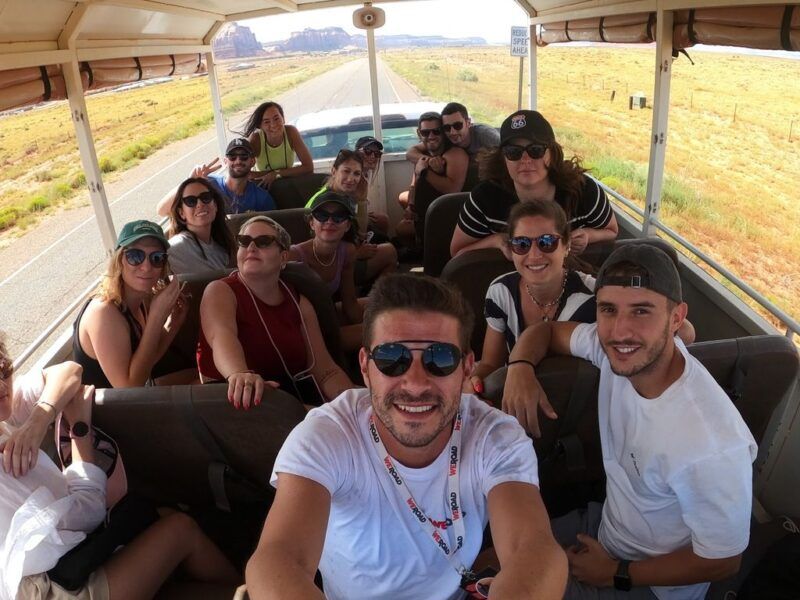 A group of WeRoad travelers taking a smiling selfie inside an open-top tour bus while traveling through a desert landscape in Canada.
