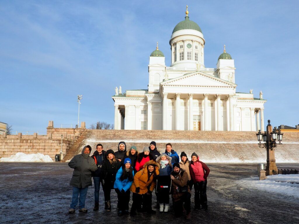 A group of WeRoad travelers posing together in front of the white Helsinki Cathedral on a bright winter day.