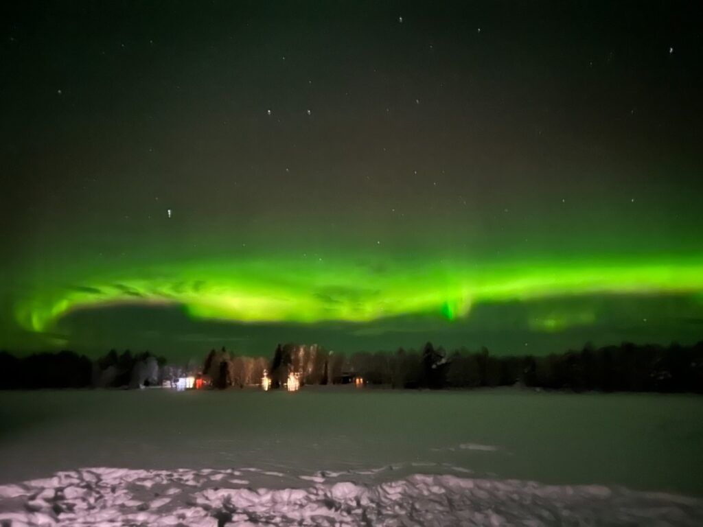 A stunning bright green Aurora Borealis stretching across the dark starry night sky over a quiet, snow-covered landscape in Lapland.