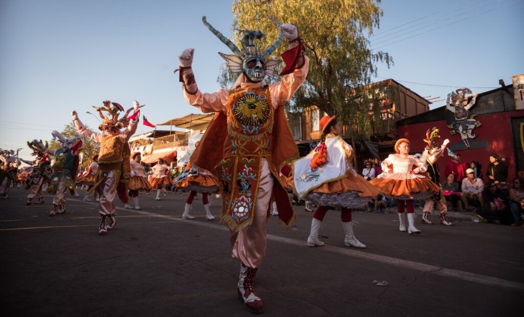 Performers in elaborate masks and vibrant costumes dancing in the street during the Fiesta de La Tirana in Chile.
