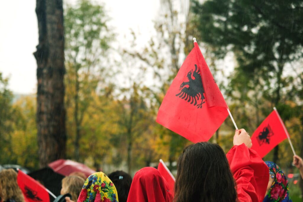 A person holding a small red Albanian flag with the black double-headed eagle.