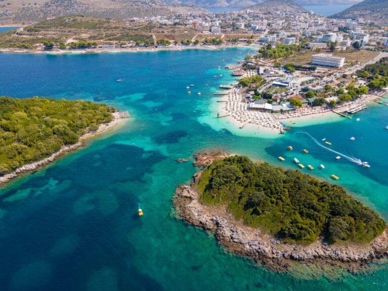 A view of the turquoise waters and white sandy beaches of Ksamil, Albania, with lush green islands and coastal resorts.