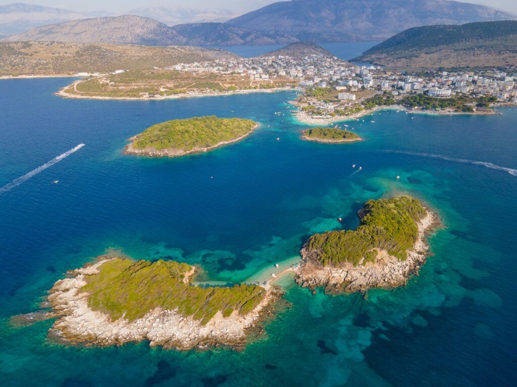 The three lush green islands of Ksamil, Albania, surrounded by vibrant turquoise water in a bright blue sea.