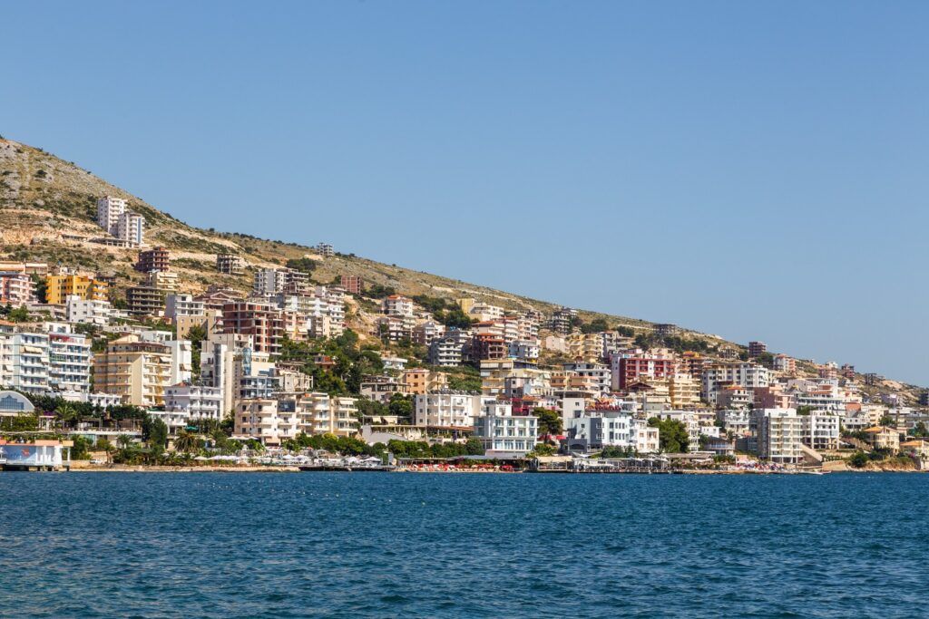 The coastal city of Saranda, Albania, with numerous white and colorful apartment buildings overlooking the deep blue sea.