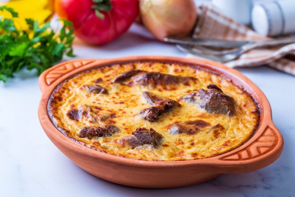 A traditional Albanian Tavë Kosi, a baked lamb and rice dish with a golden yogurt crust, served in a rustic clay pot.