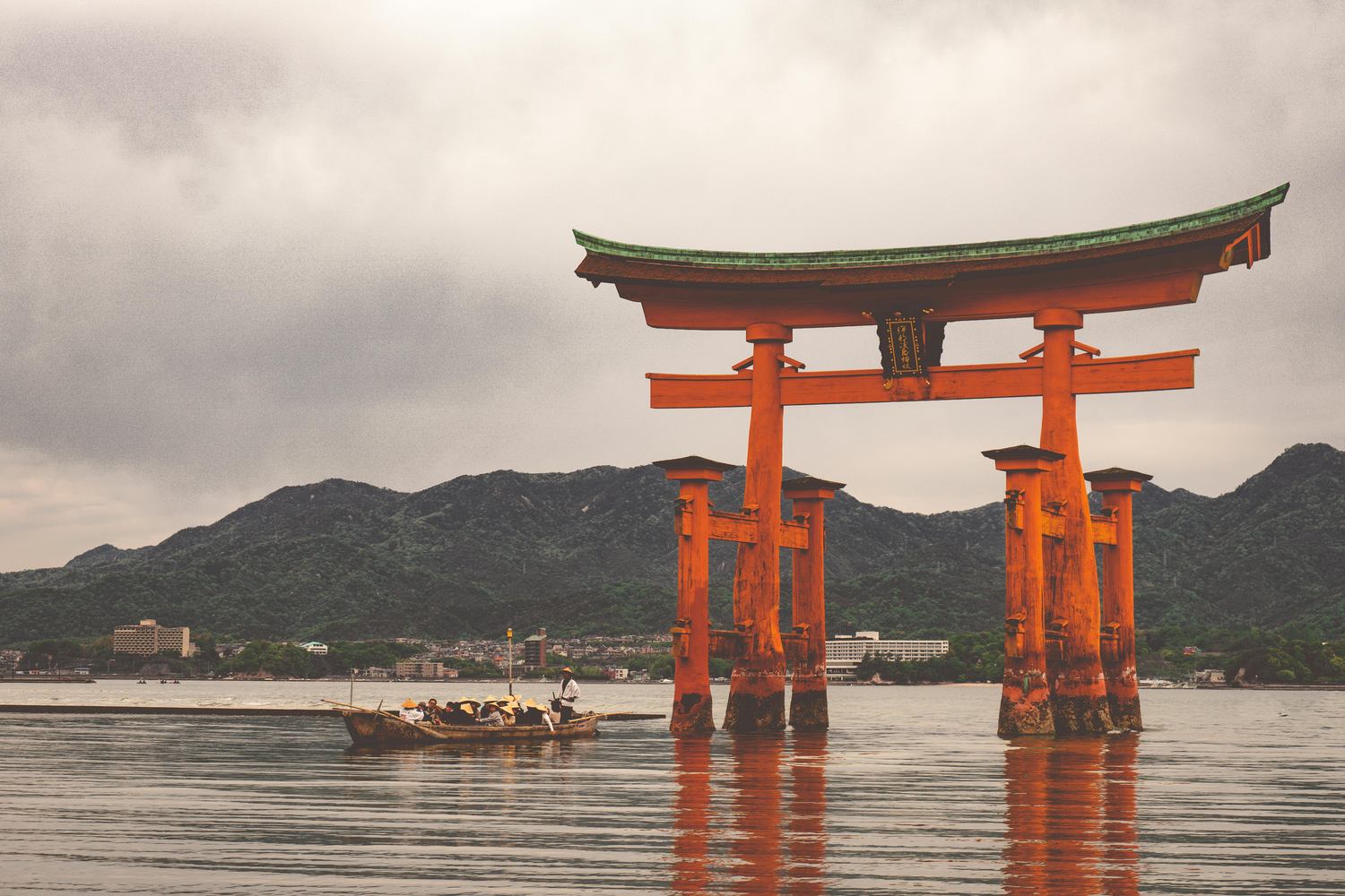 Red floating torii gate of Itsukushima Shrine in the sea at Miyajima, Japan, with a small boat and misty mountains behind