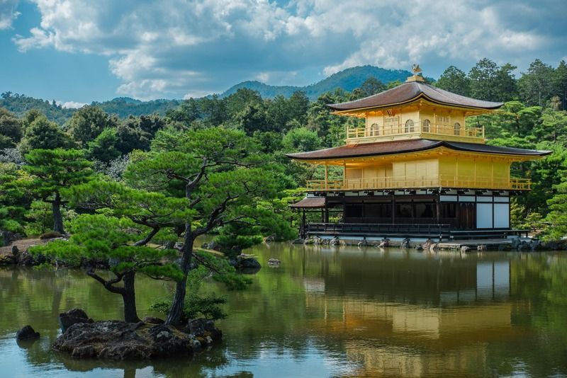 Kinkaku-ji Golden Pavilion reflected in Kyoko-chi pond, framed by pine trees and green hills in Kyoto, Japan