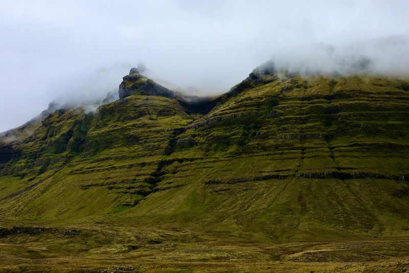 Green layered basalt mountains wrapped in low clouds over a wild Icelandic landscape