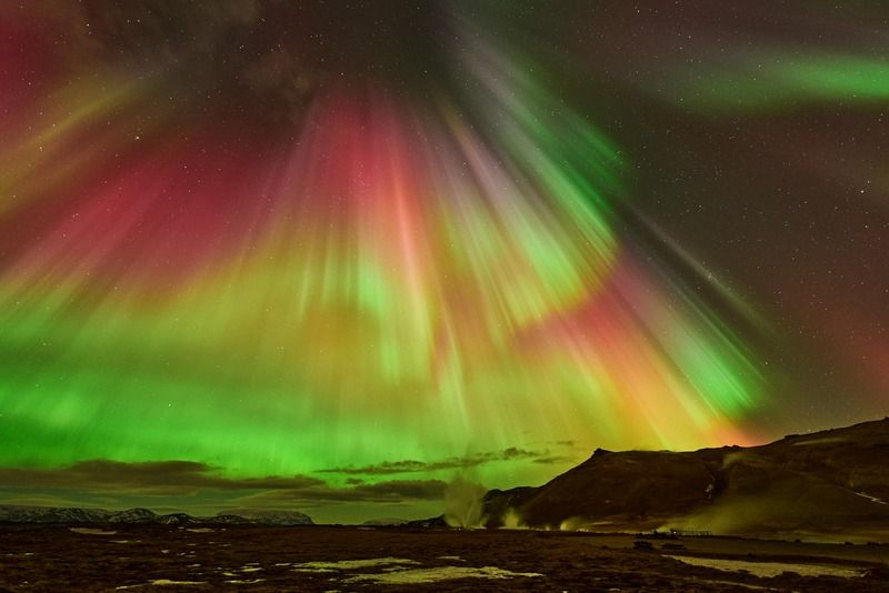 Northern lights with red, green and yellow hues over a snowy mountain landscape at night
