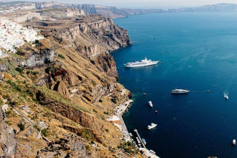 erial view of Santorini's caldera with white clifftop buildings of Fira and cruise ships anchored in the deep blue Aegean Sea erial view of Santorini's caldera with white clifftop buildings of Fira and cruise ships anchored in the deep blue Aegean Sea