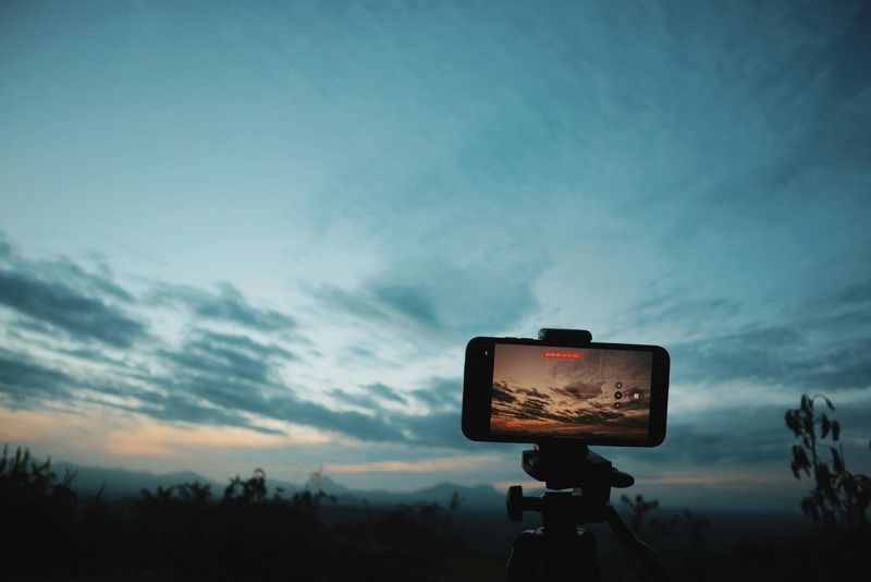 "Smartphone mounted on a tripod recording a cloudy sunset sky over a mountain landscape"