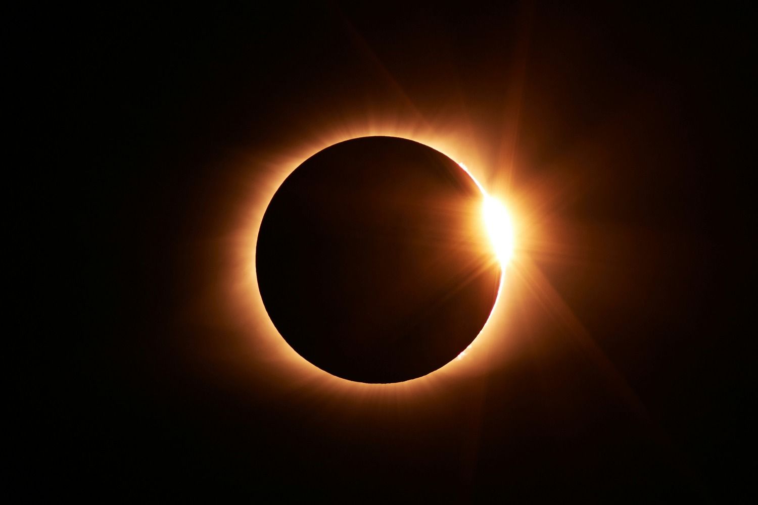 Total solar eclipse with diamond ring effect, bright corona glowing around the moon against a dark sky