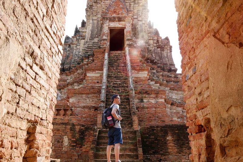 Backpacker with a daypack standing at the base of ancient brick temple ruins in Southeast Asia, gazing up at the towering stone structure