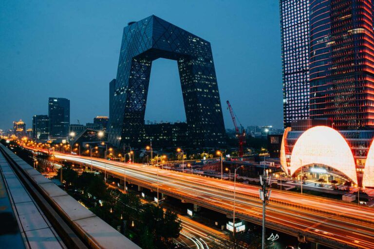 Beijing's CCTV Headquarters building illuminated at night with glowing traffic light trails streaking along the highway below