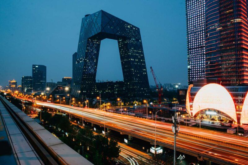 Beijing's CCTV Headquarters building illuminated at night with glowing traffic light trails streaking along the highway below Beijing's CCTV Headquarters building illuminated at night with glowing traffic light trails streaking along the highway below