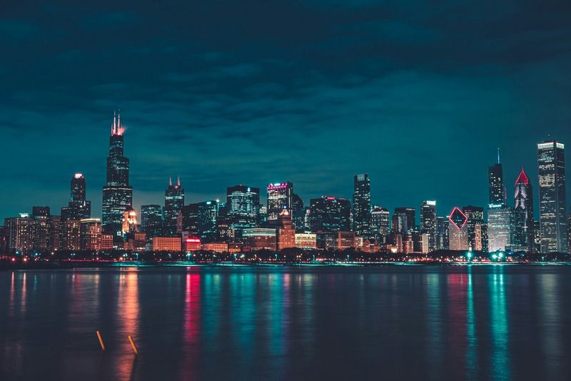 Chicago skyline at night seen from Lake Michigan, with Willis Tower and downtown skyscrapers lit up in colorful lights reflecting on the water