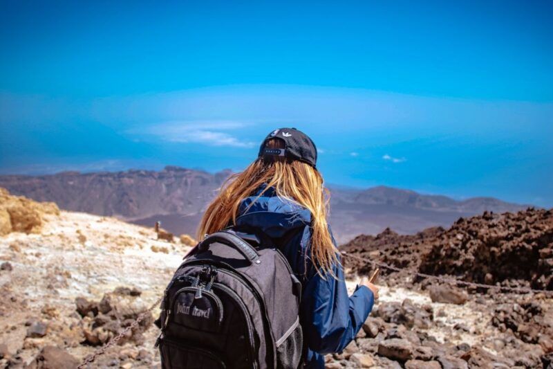 Back view of a woman hiking in a rugged volcanic landscape under a clear blue sky.