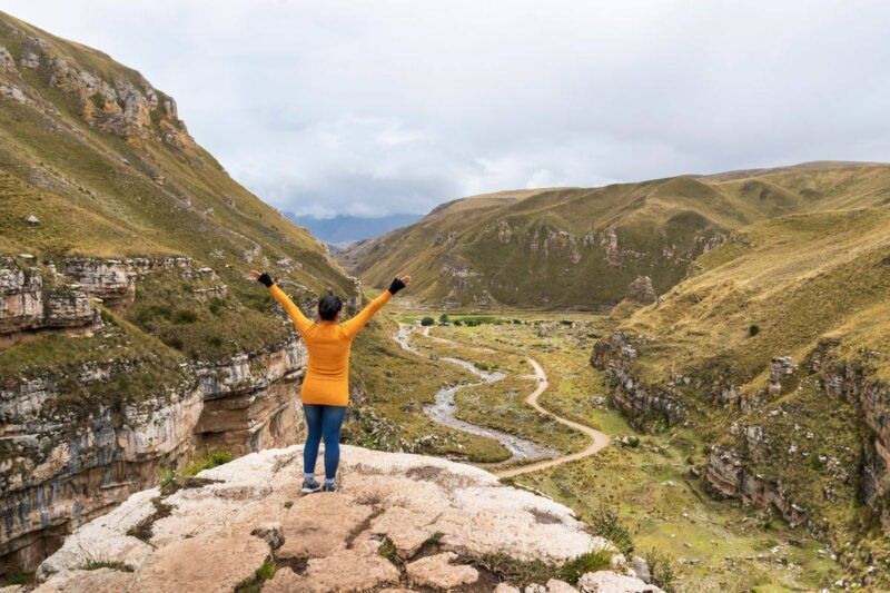 Woman stands with arms raised on a cliff in Jauja's scenic canyon.