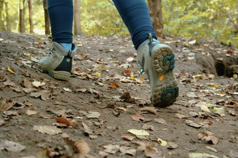 Close-up of hiking boots walking on a dirt trail covered in autumn leaves in a forest