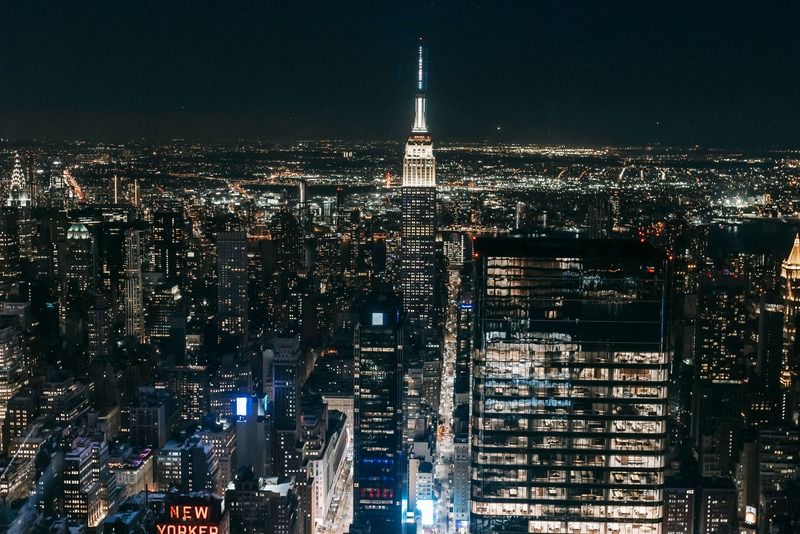Aerial night view of the New York City skyline with the Empire State Building illuminated at the center and the New Yorker sign visible below