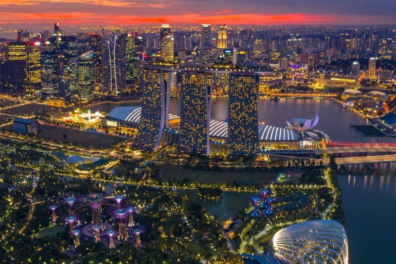 Aerial view of Singapore's Marina Bay skyline at sunset, with Gardens by the Bay's illuminated Supertrees in the foreground