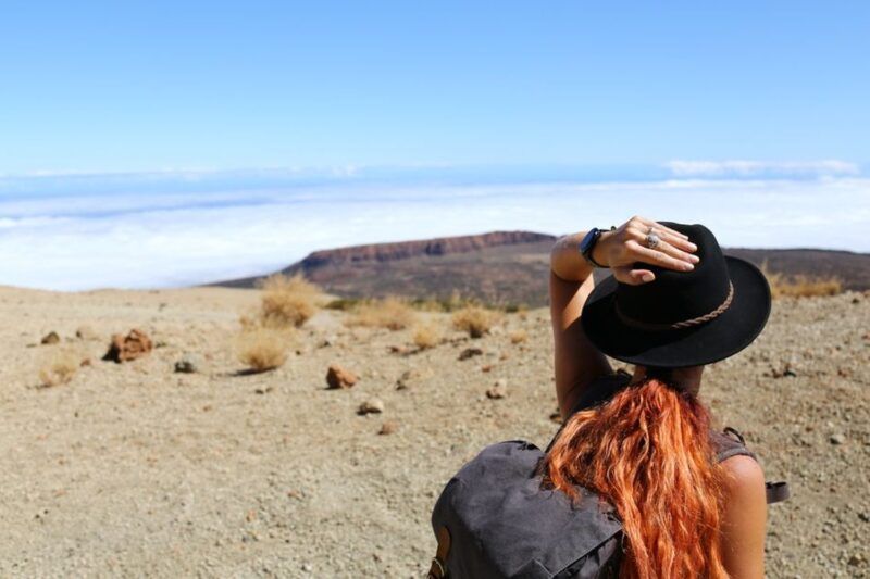 Woman with a backpack looking out over a volcanic desert landscape rising above the clouds on a sunny day