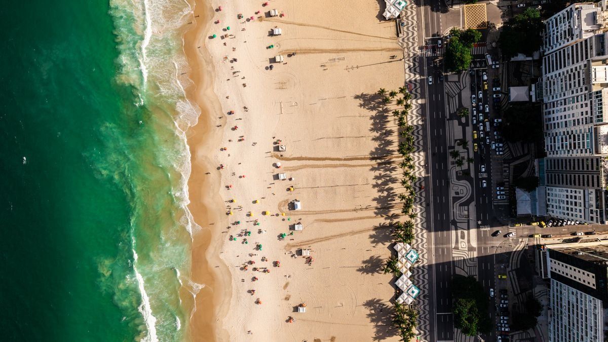 Aerial view of Copacabana Beach with ocean waves, sunbathers, palm shadows, and city buildings