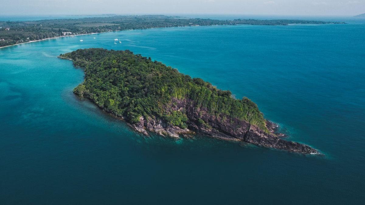 Aerial view of a forested island surrounded by clear blue sea