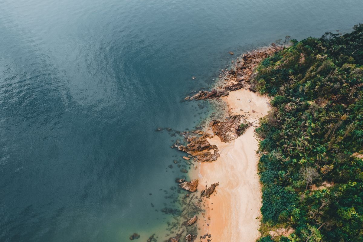 Aerial view of a quiet sandy beach with rocky edges and dense tropical greenery