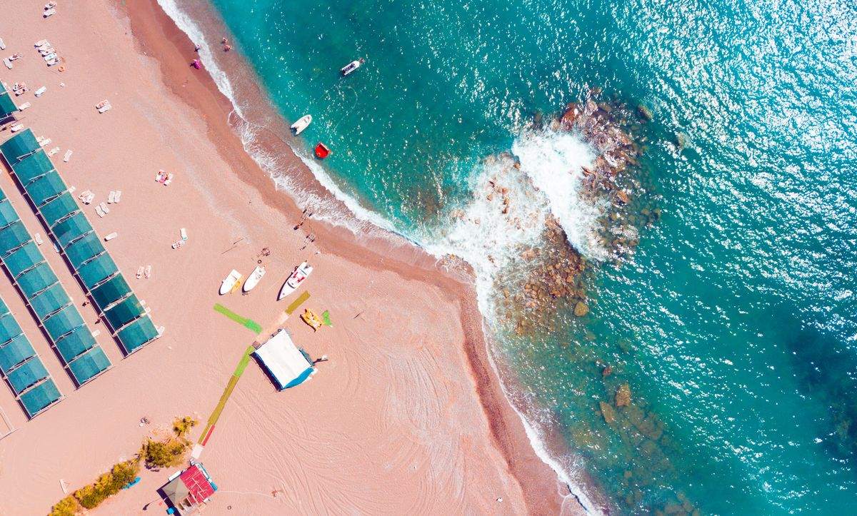 Aerial view of a sandy beach with small boats, clear water, and waves breaking over rocks