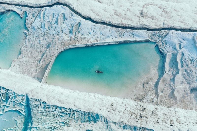 Aerial view of turquoise travertine pools in Pamukkale with a person swimming