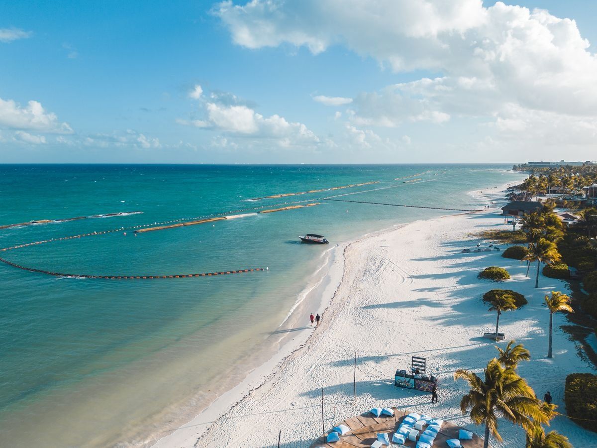 Aerial view of a white sand beach with turquoise water, palm trees, and a small boat offshore