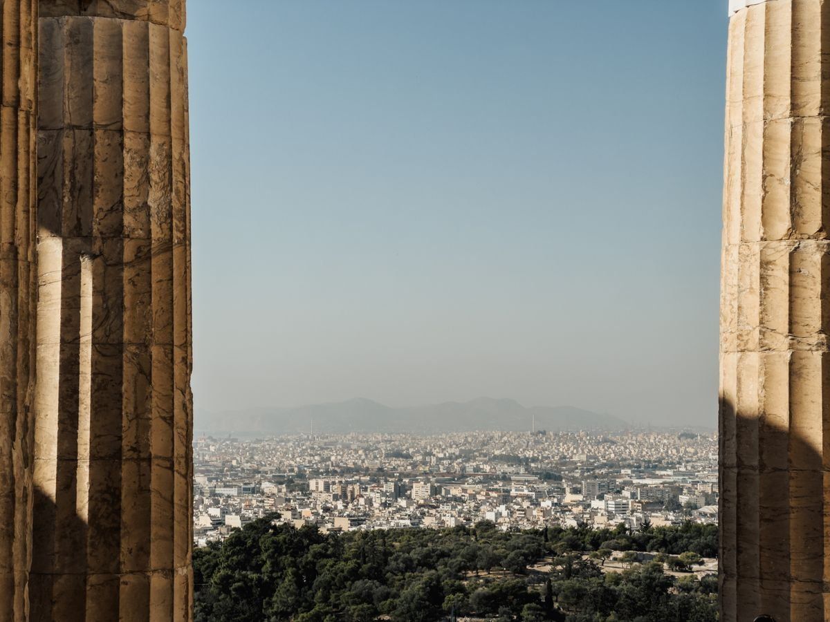Athens skyline seen between two ancient stone columns above a green hillside