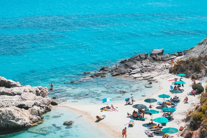 Sunbathers and beach umbrellas along a rocky cove with crystal-clear turquoise water in Greece