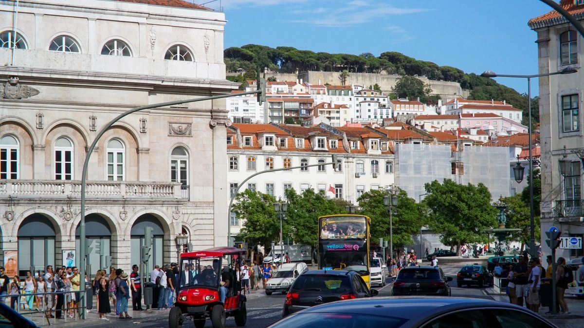 Busy Lisbon street with cars, a tuk tuk, and hillside buildings in the background