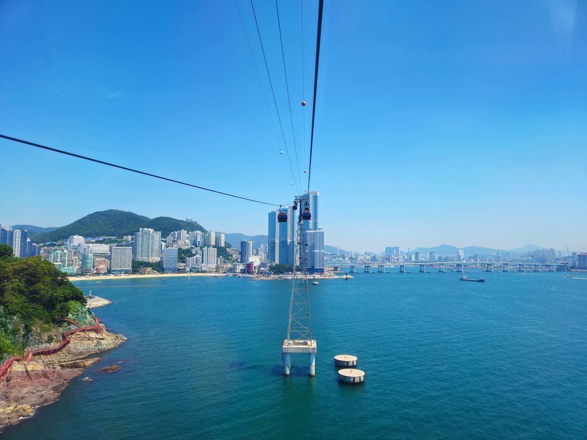 Cable car lines stretching above blue water toward Busan high-rises and a distant bridge