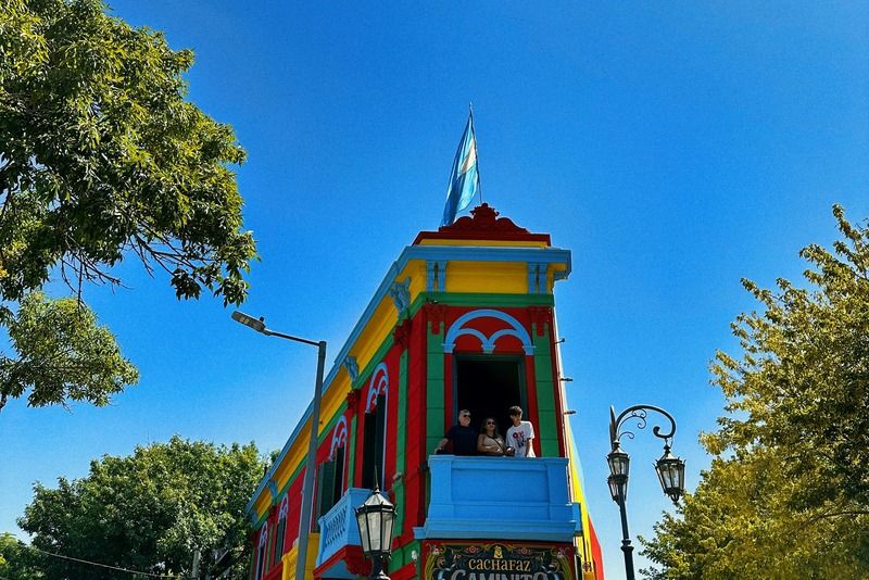 Brightly painted corner building in Caminito, Buenos Aires, with an Argentine flag on top and tourists gathered below