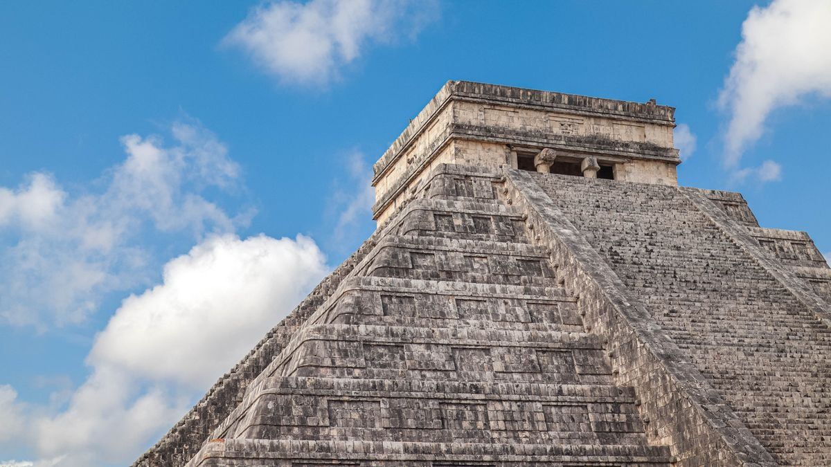 Close view of the Pyramid of Kukulcan under a bright blue sky with scattered white clouds
