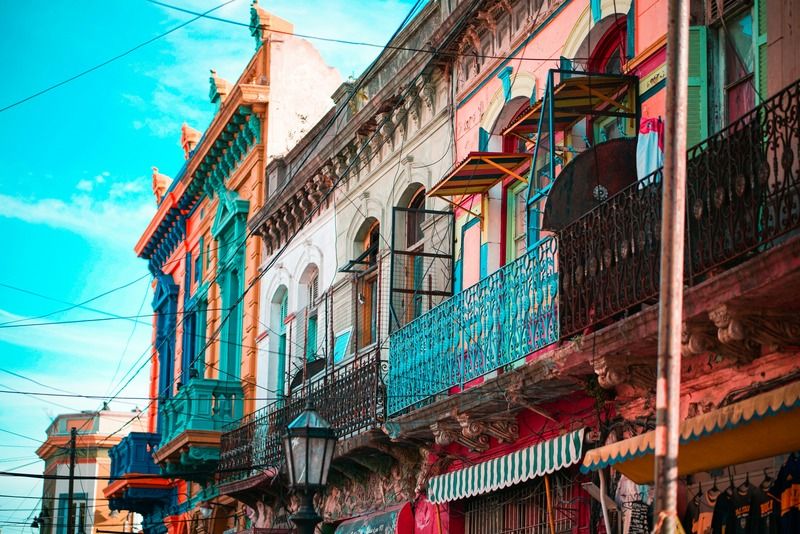 Row of ornate colonial buildings in Buenos Aires with turquoise wrought-iron balconies and striped awnings under a blue sky