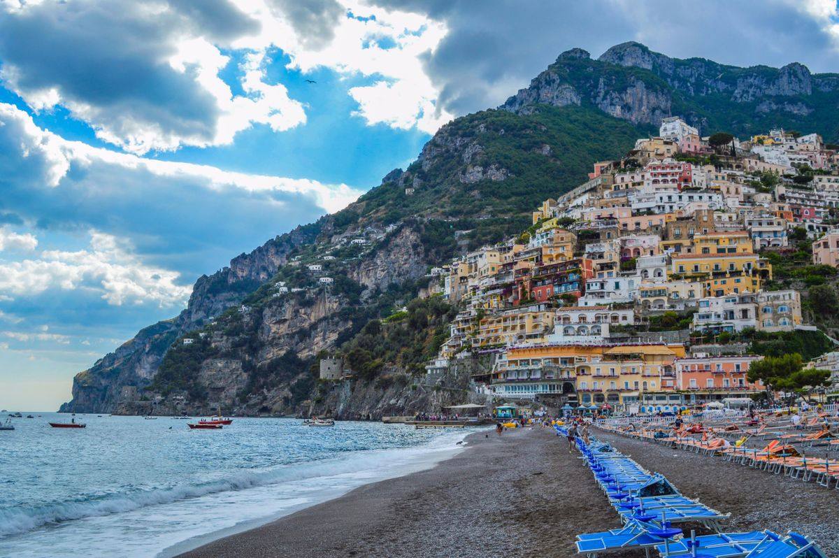 Colorful hillside houses in Positano above a dark pebble beach and calm sea