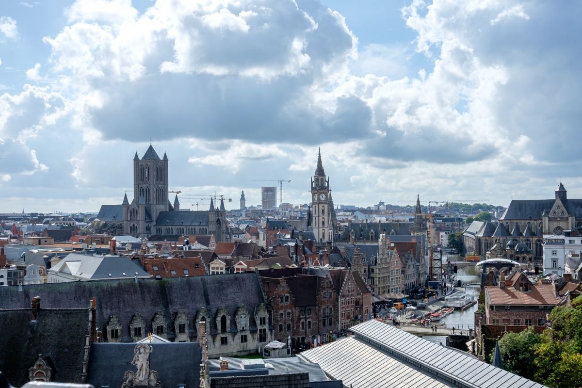 Ghent skyline with church towers, historic rooftops, and dramatic clouds overhead