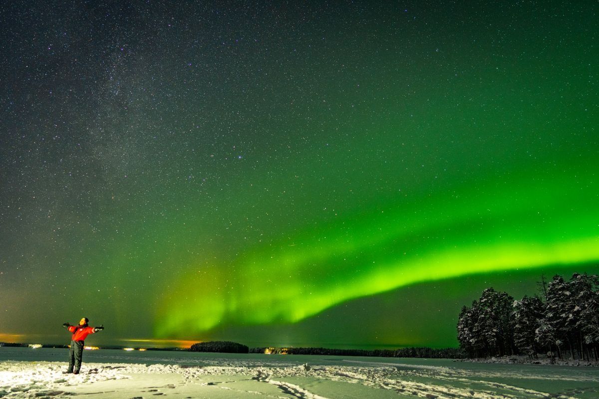 Green northern lights over a snowy field with a person standing under the night sky