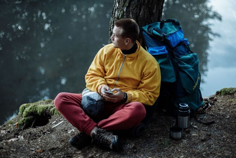 Hiker taking a break by a lake with a backpack and thermos during a hiking trip