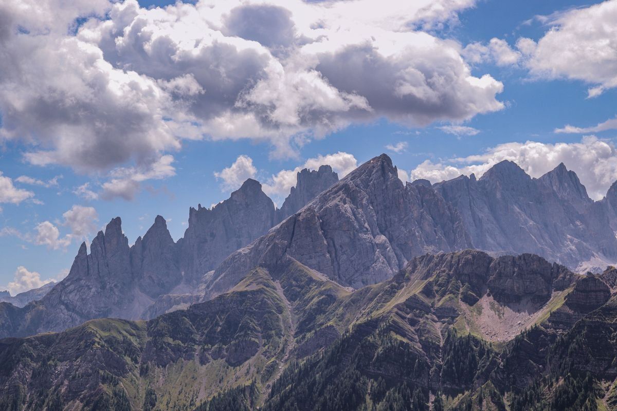 Jagged Dolomite mountain range beneath a bright blue sky with large drifting clouds