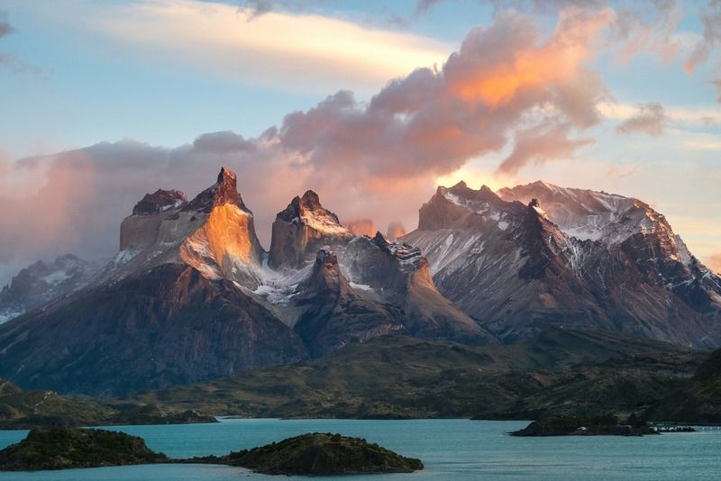 Jagged mountain peaks glowing at sunset above a glacial lake dotted with small green islands