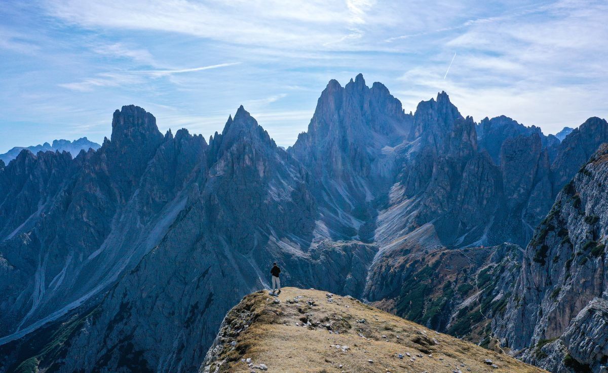 Lone hiker on a rocky ridge facing towering jagged peaks in the Dolomites